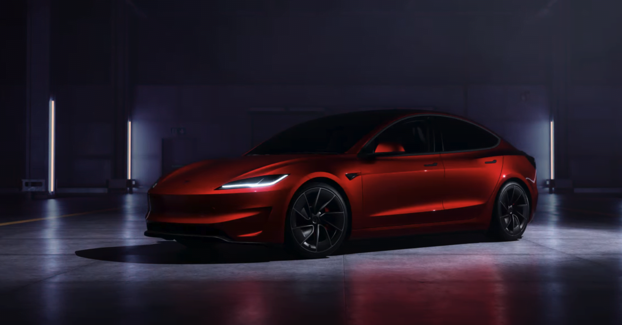 Tesla Model 3 Performance. Czerwony elektryczny samochód sportowy w zaciemnionym garażu, oświetlonym pionowymi światłami LED.