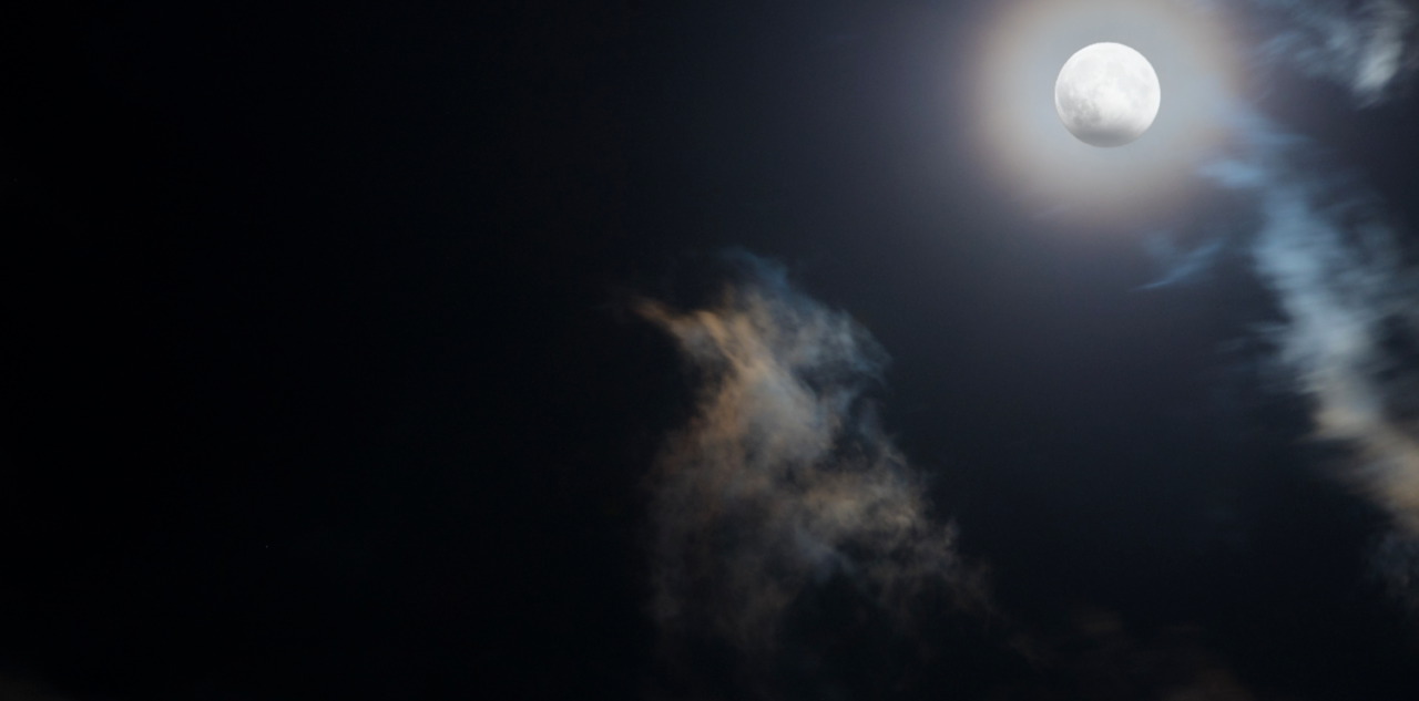 Pełnia księżyca na nocnym niebie z prześwitującymi chmurami.