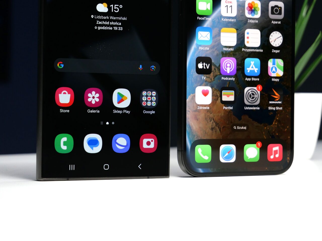 Dwa smartfony postawione obok siebie na biurku, z lewej telefon z interfejsem Android i wyświetlonymi aplikacjami, z prawej iPhone z otwartym ekranem głównym i ikonami aplikacji iOS.