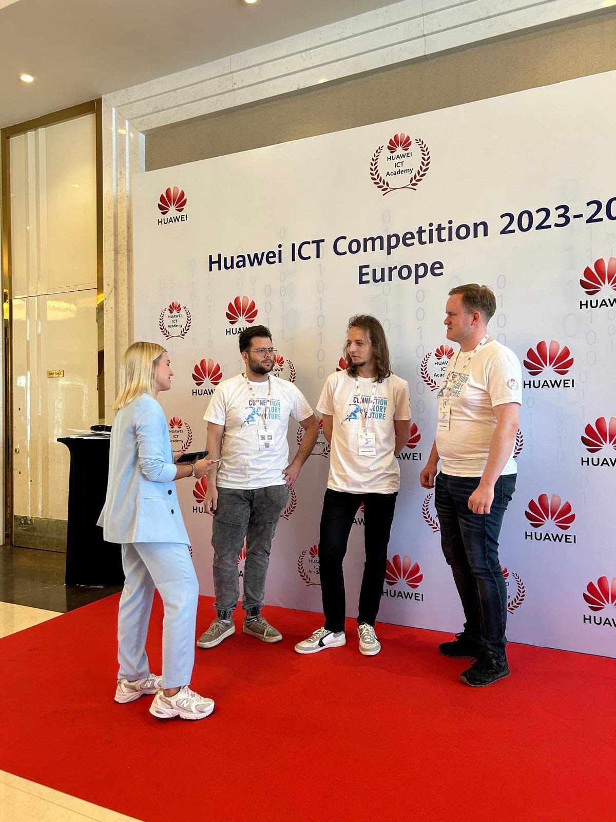 Cztery osoby rozmawiają przed ścianką reklamową z logo Huawei podczas Europejskich Zawodów ICT Huawei 2023-2024.