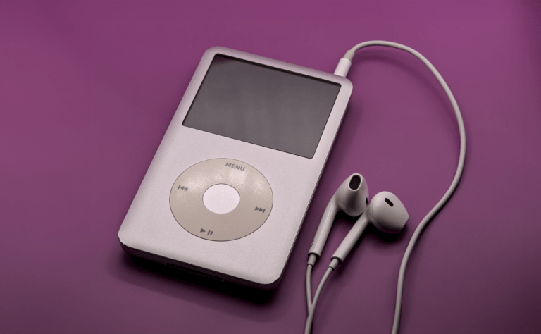 Srebrny odtwarzacz muzyki typu MP3 z białymi słuchawkami na fioletowym tle.