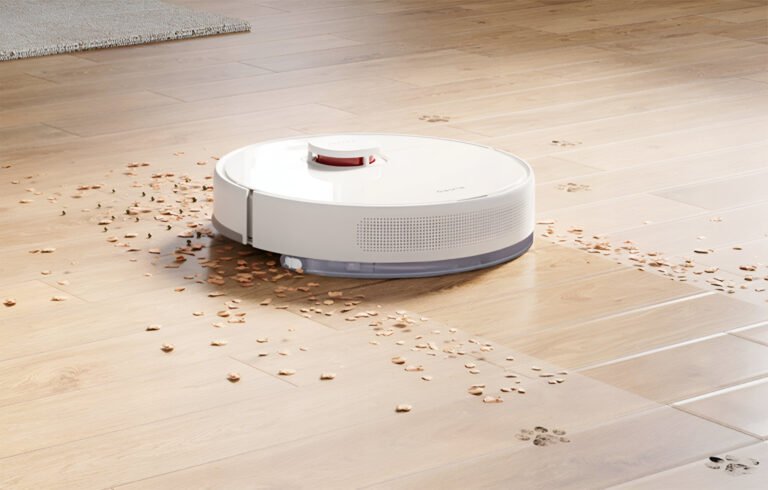 Robot sprzątający Dreame na podłodze, z którego zbiera okruchy i liście, widać także ślady brudu lub błota.