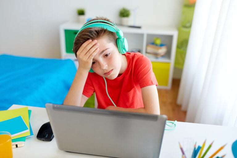 Zaniepokojony chłopiec w czerwonej koszulce i zielonych słuchawkach na głowie, siedzący przed laptopem i trzymający rękę na czole, w jasnym pokoju. Legendarny twórca Tekkena wie, dlaczego boi się przegranej