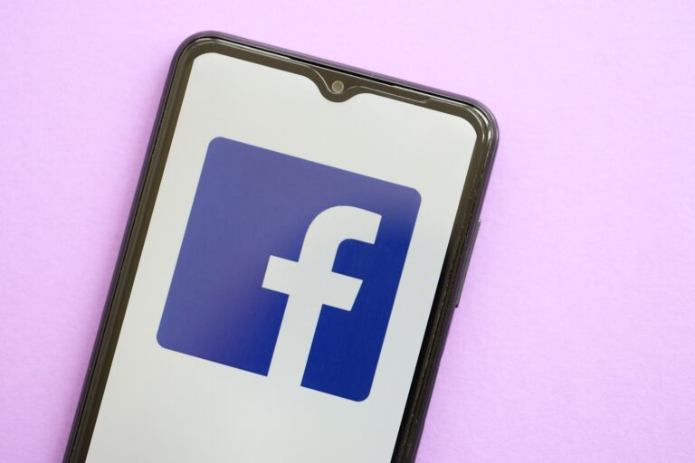 Smartfon na jasnofioletowym tle z ekranem pokazującym logo Facebooka.