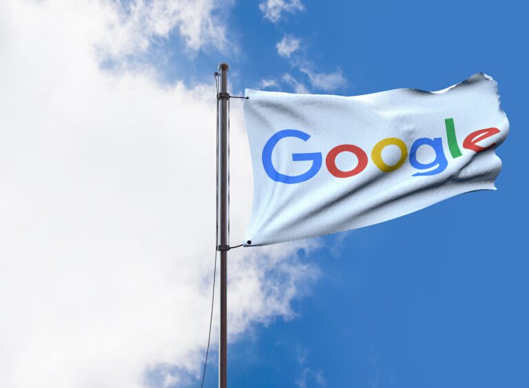 Flaga Google powiewająca na tle niebieskiego nieba z chmurami.