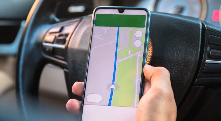 Ręka trzymająca smartfon z włączoną aplikacją nawigacyjną w samochodzie.