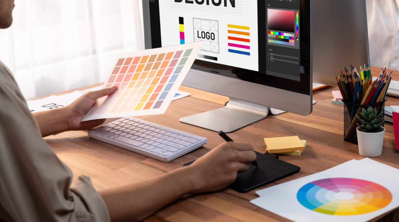 Projektant graficzny pracujący przy komputerze i wybierający kolory z próbnika barw.