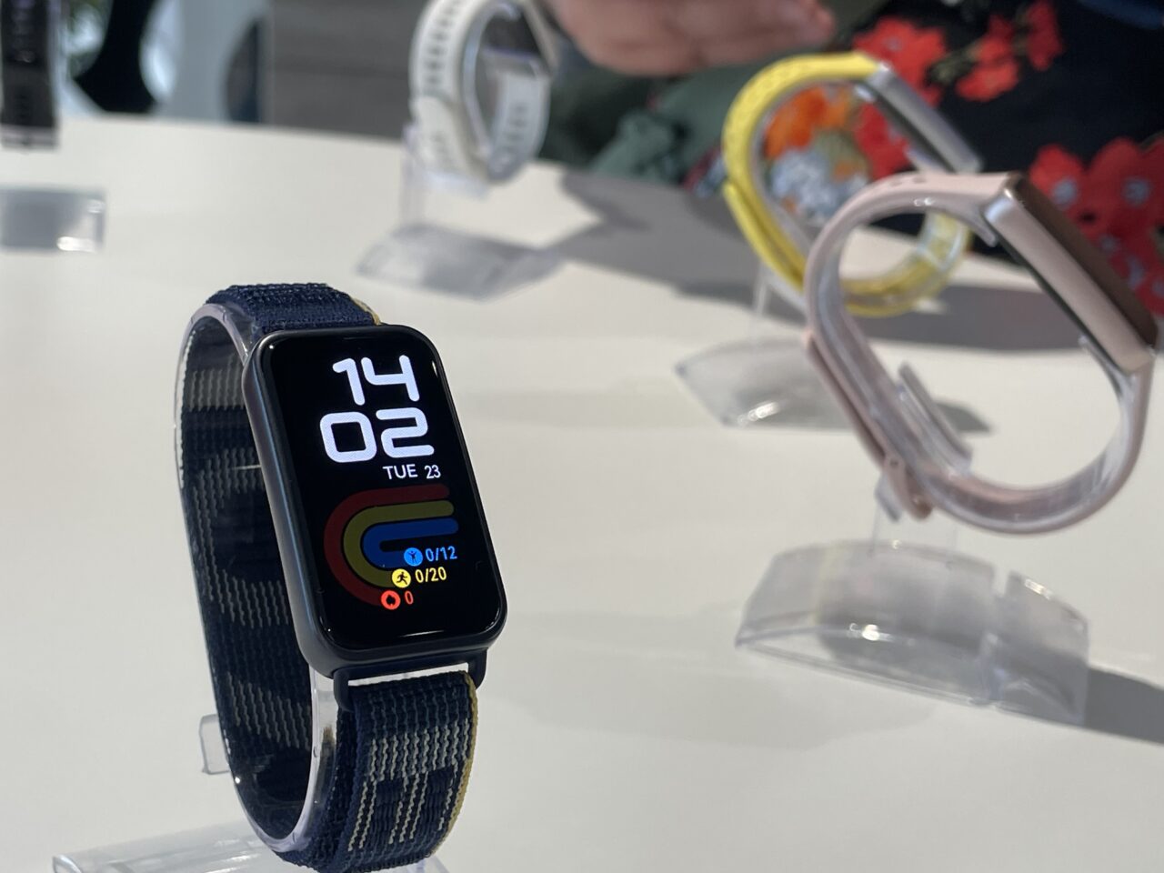Smartwatch na nadgarstku z niebieskim paskiem, pokazujący czas i aktywność, na tle innych zegarków.