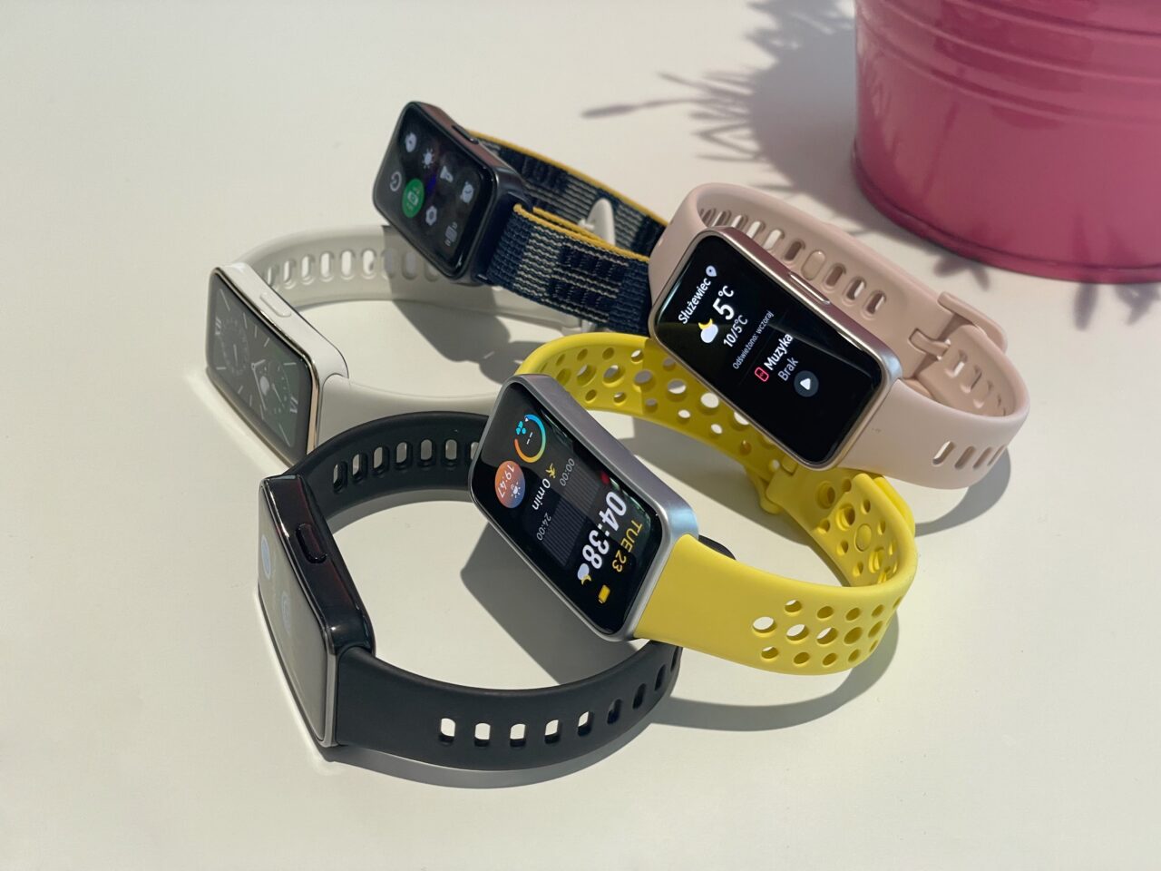 Cztery inteligentne zegarki z różnokolorowymi paskami leżące na białym stole.