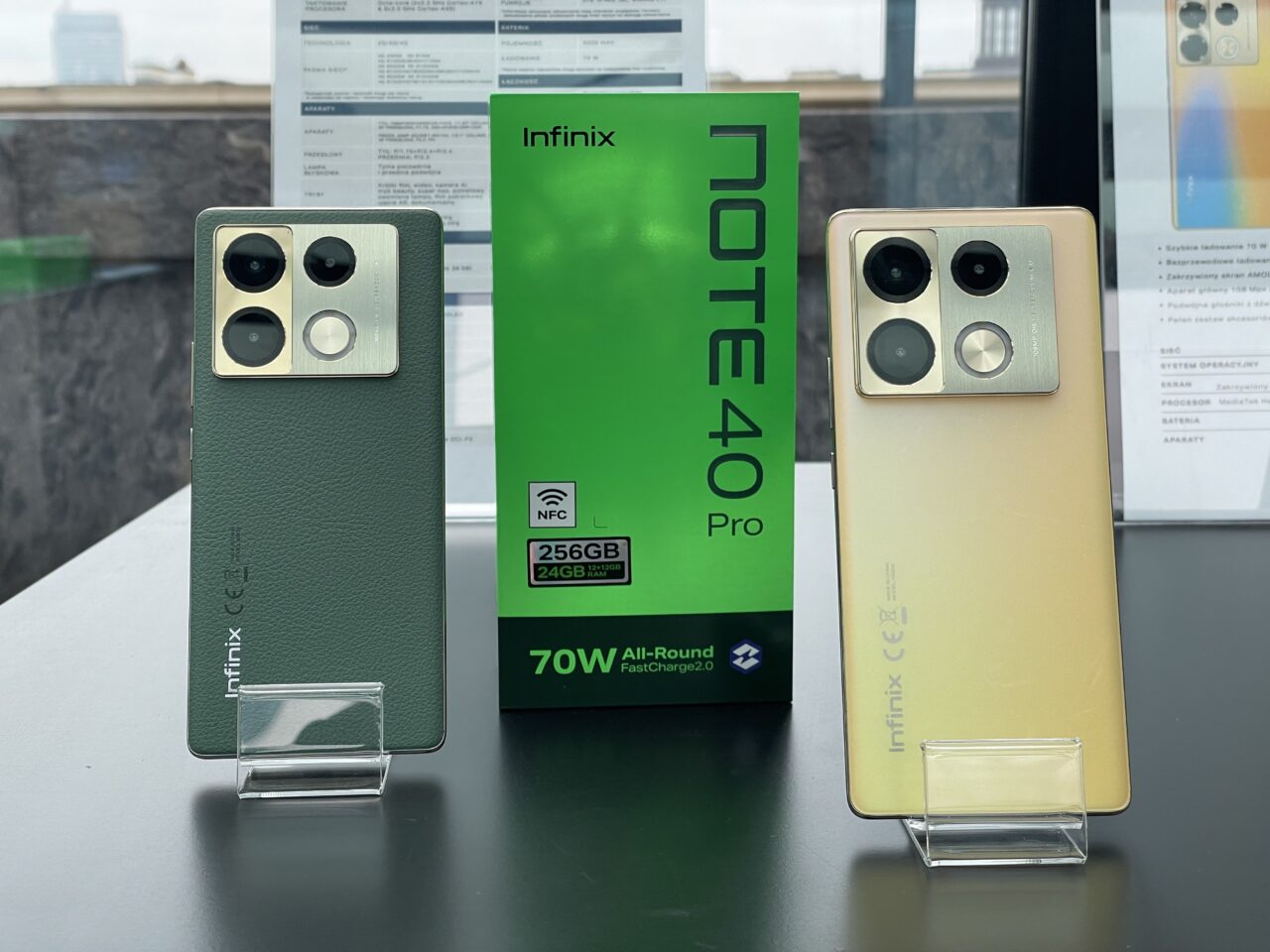 Dwa smartfony Infinix na stojakach z pudełkiem Infinix Note 40 Pro w tle, jeden koloru złotego, drugi zielony.