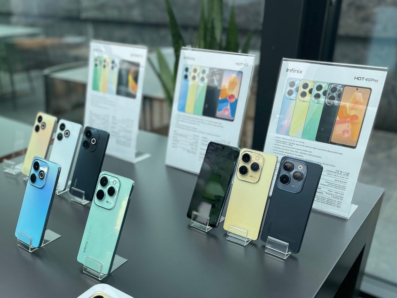 Wystawa smartfonów Infinix w różnych kolorach, ustawiona na przeszklonej ladzie, z informacyjnymi ulotkami w tle.