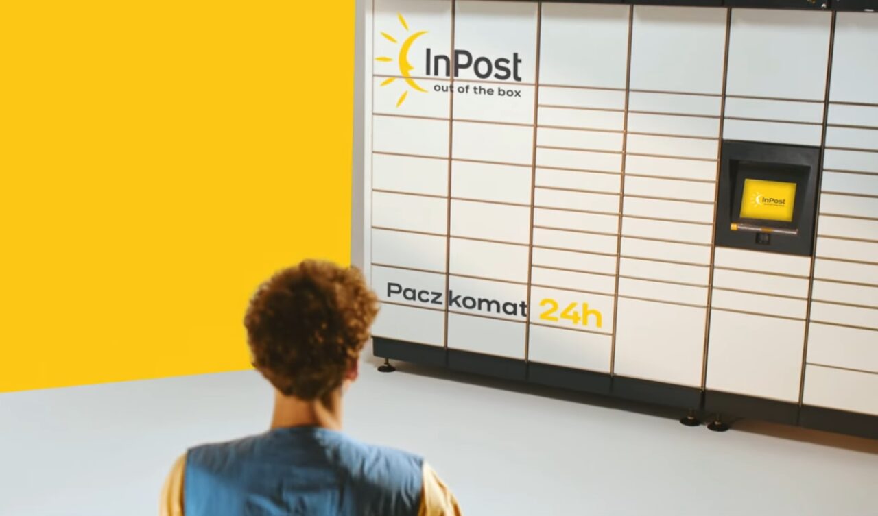 Osoba stojąca przed paczkomatem InPost 24h na żółtym tle.