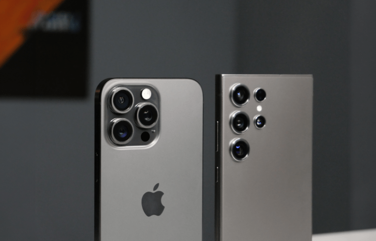Tylna strona dwóch smartfonów z potrójnymi aparatami ustawionymi obok siebie, po lewej stronie smartfon z logiem nadgryzionego jabłka, po prawej z sześcioma obiektywami w dwóch kolumnach.