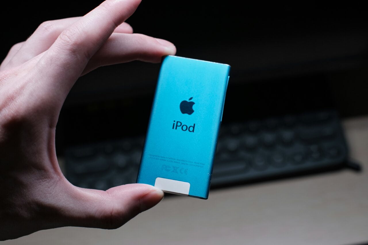 Ręka trzymająca niebieski iPod Shuffle firmy Apple na tle klawiatury komputerowej.