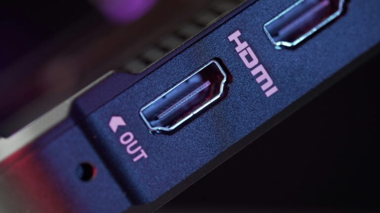 Zbliżenie na niebieski kabel HDMI z napisem 'OUT' na urządzeniu elektronicznym z lekkim czerwono-fioletowym odbiciem w tle.