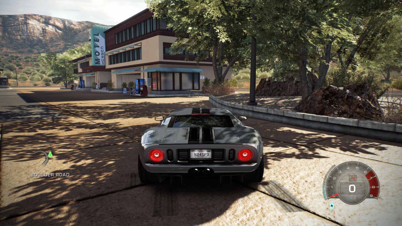 Srebrna Wyscigowa Samochód stoi na parkingu przed budynkiem kinowym "Le Coupres" w wirtualnym świecie gry, w tle widoczne góry i drzewa.