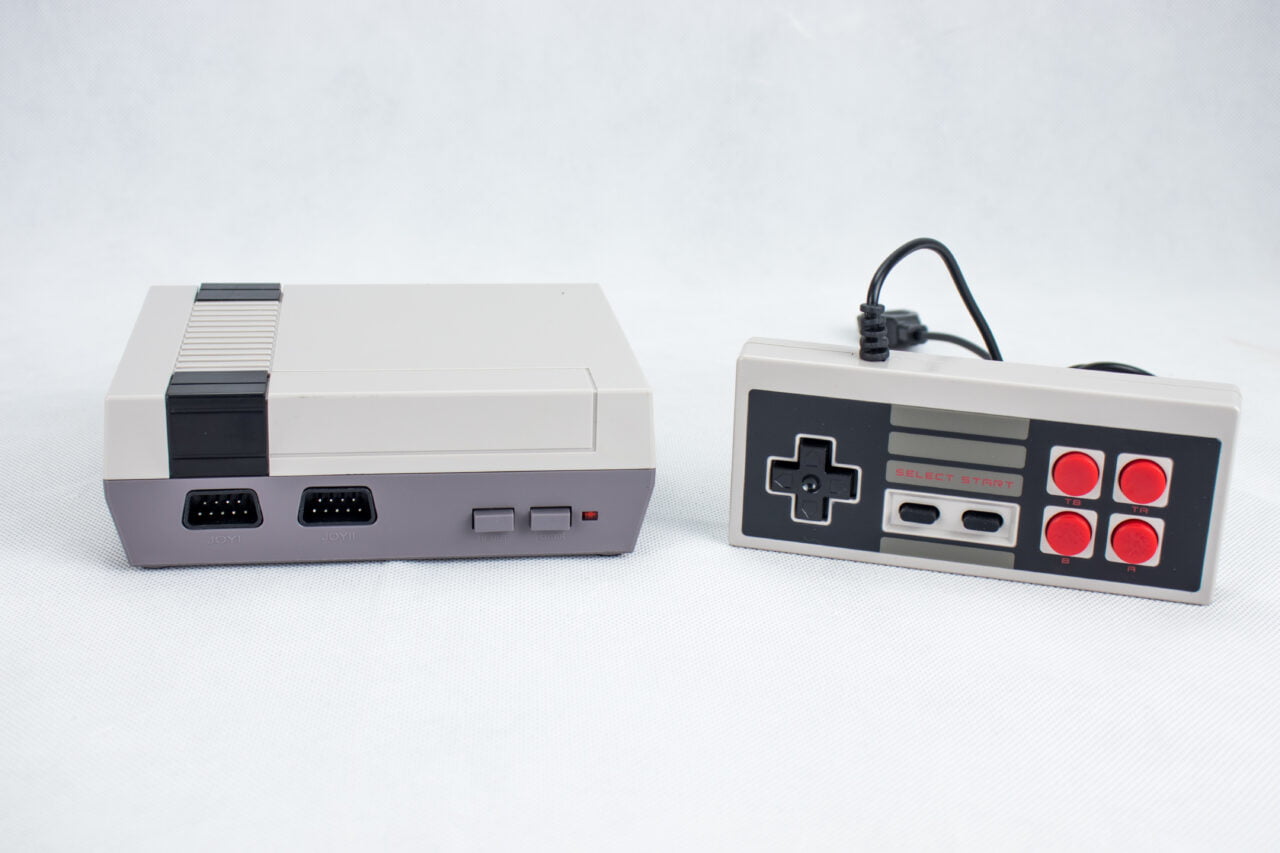 Konsola do gier Nintendo Entertainment System z lat 80. i jej kontroler przewodowy, na białym tle.