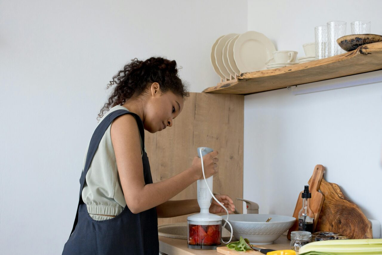Kobieta używa blendera ręcznego do miksowania składników w kuchni.