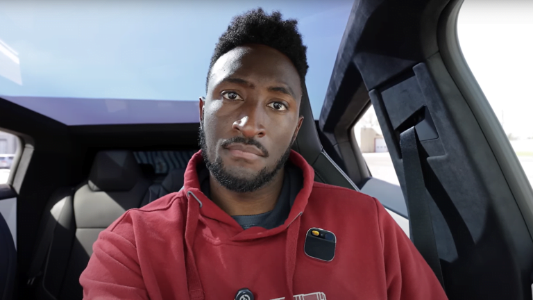 Mężczyzna siedzący na przednim siedzeniu samochodu wykonuje selfie; ma na sobie czerwoną bluzę i patrzy poważnie w kamerę.