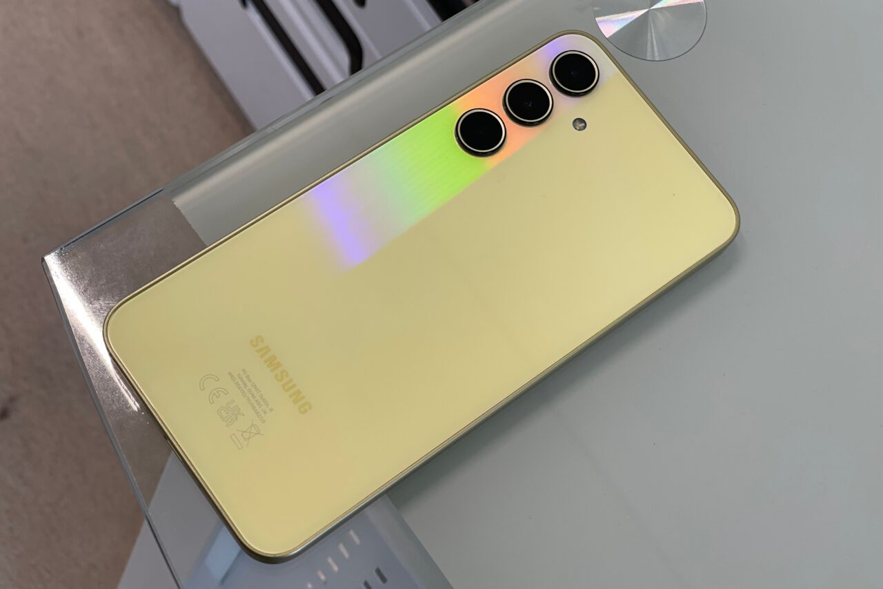 Żółty smartfon Samsung z potrójnym aparatem umieszczonym po lewej stronie, leżący na szklanym blacie.