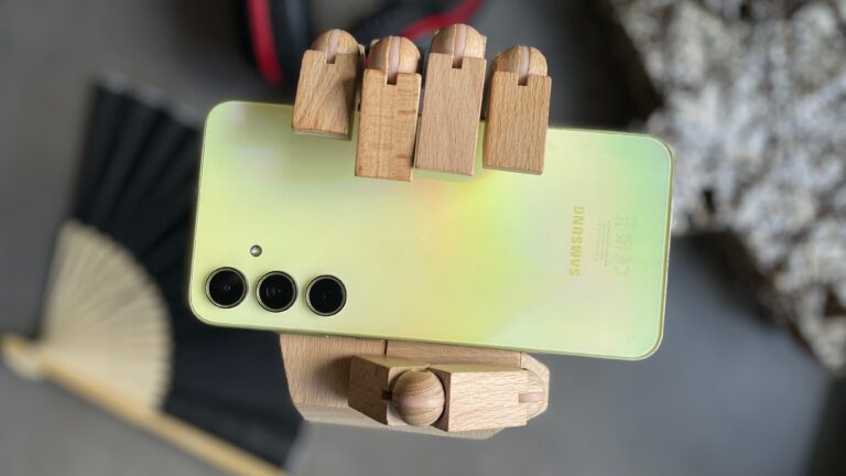 Drewniana ręka trzymająca żółtozielony smartfon Samsung z potrójnym aparatem.