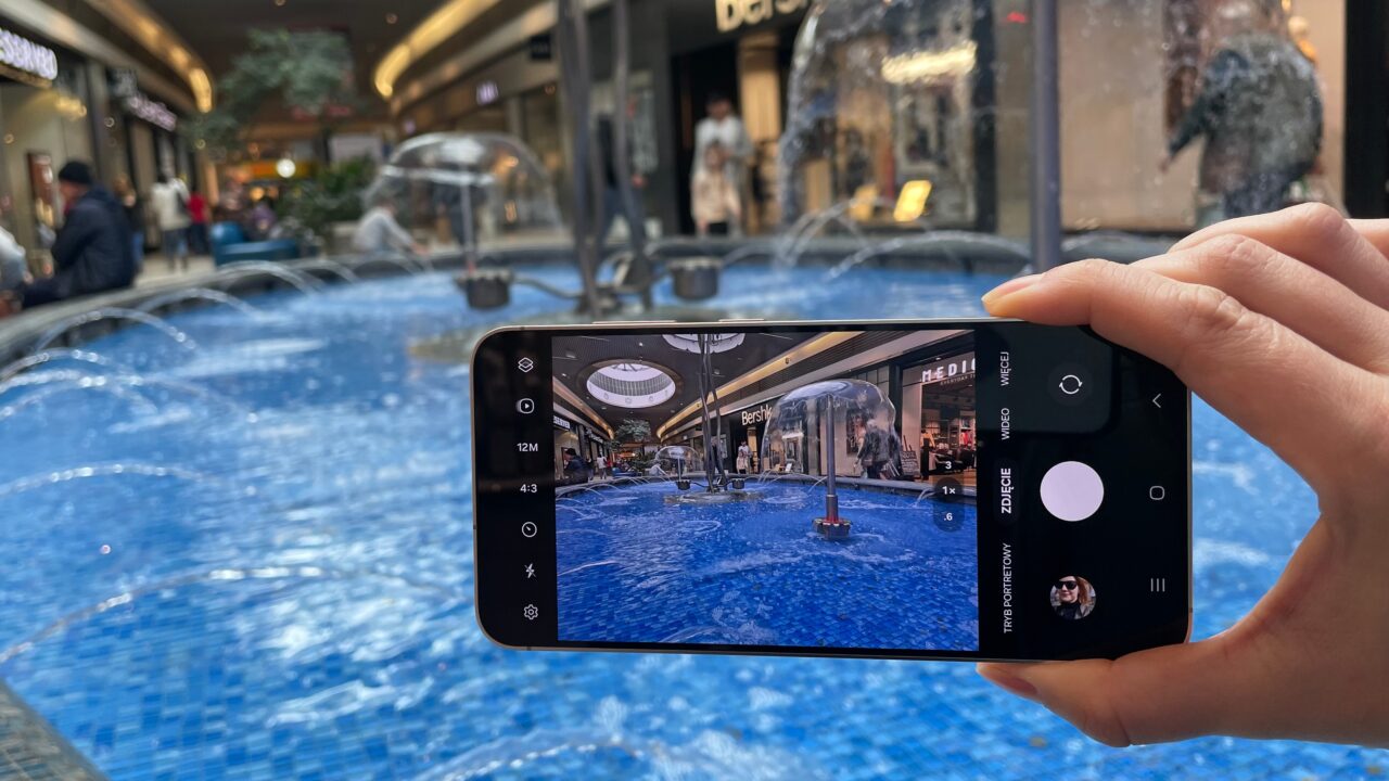 Ręka trzymająca smartfon, który fotografuje fontannę w centrum handlowym.