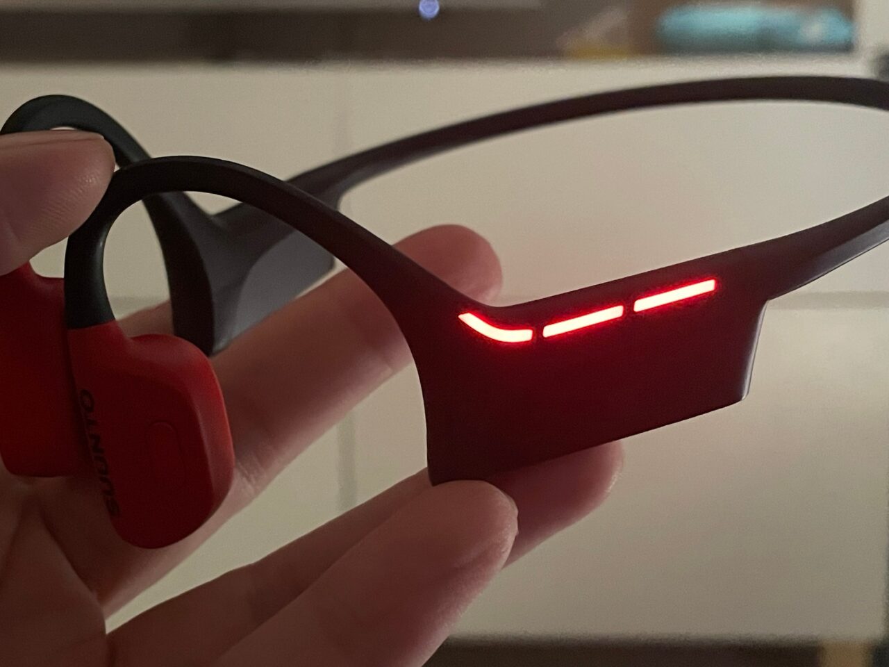 Czerwone słuchawki sportowe trzymane w dłoni, z podświetleniem LED na pałąku.