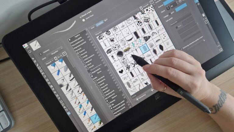 Osoba pracuje na cyfrowym tablecie graficznym używając rysika, pokazując ekran z interfejsem programu do grafiki z wyborem różnych pędzli i narzędzi.