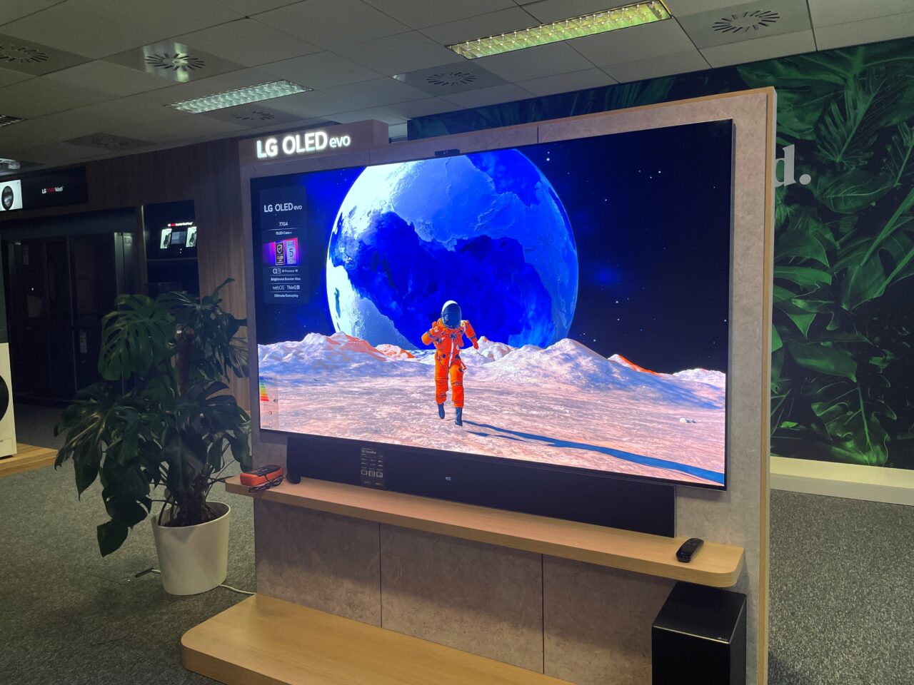 Telewizor LG OLED Evo wyświetlający obraz astronauty na tle wielkiego księżyca i pejzażu kosmicznego, ustawiony w nowoczesnym pomieszczeniu z roślinami.