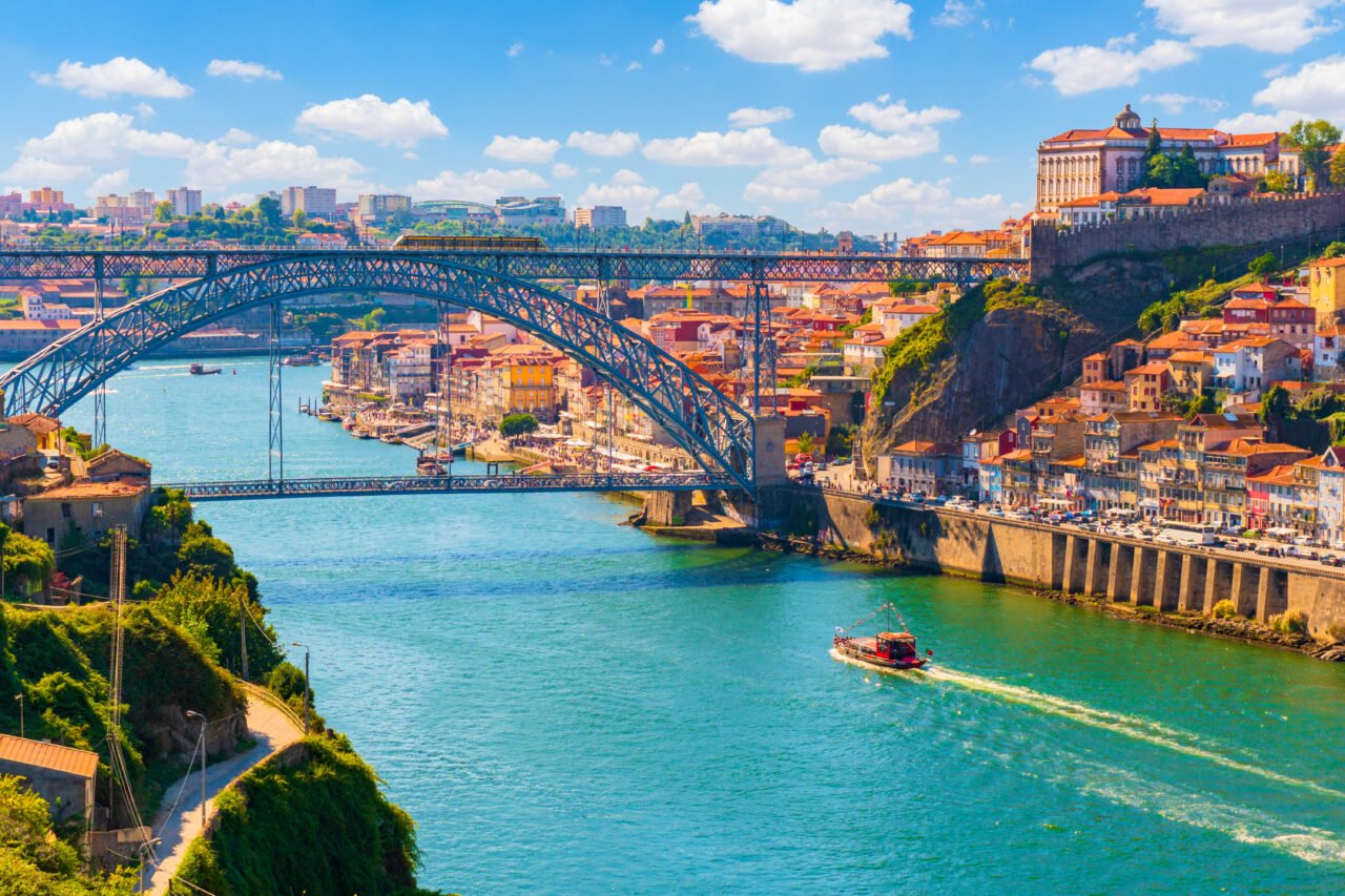 Widok na Most Dom Luís I nad rzeką Duero w Porto, otoczony kolorowymi zabudowaniami i żeglującymi łodziami
