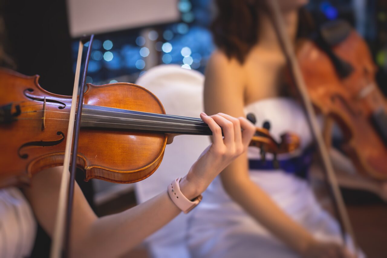 Kobieta gra na skrzypcach w oświetlonym wnętrzu z rozmazanymi światełkami w tle.