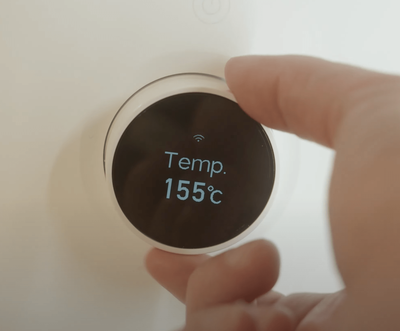Uma mão ajustando a temperatura em um termostato digital mostrando 155 graus Celsius.