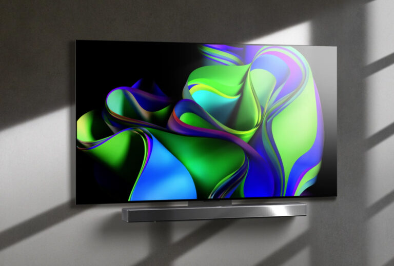 Nowoczesny telewizor LG wyświetlający kolorową, abstrakcyjną grafikę na ciemnym tle, umieszczony na jasnej ścianie z cieniami.