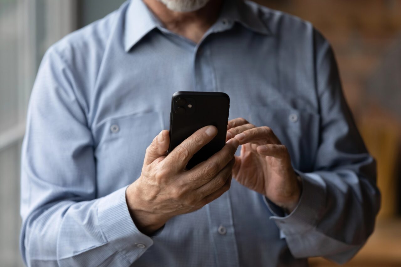 Starszy mężczyzna używa czarnego smartfona.