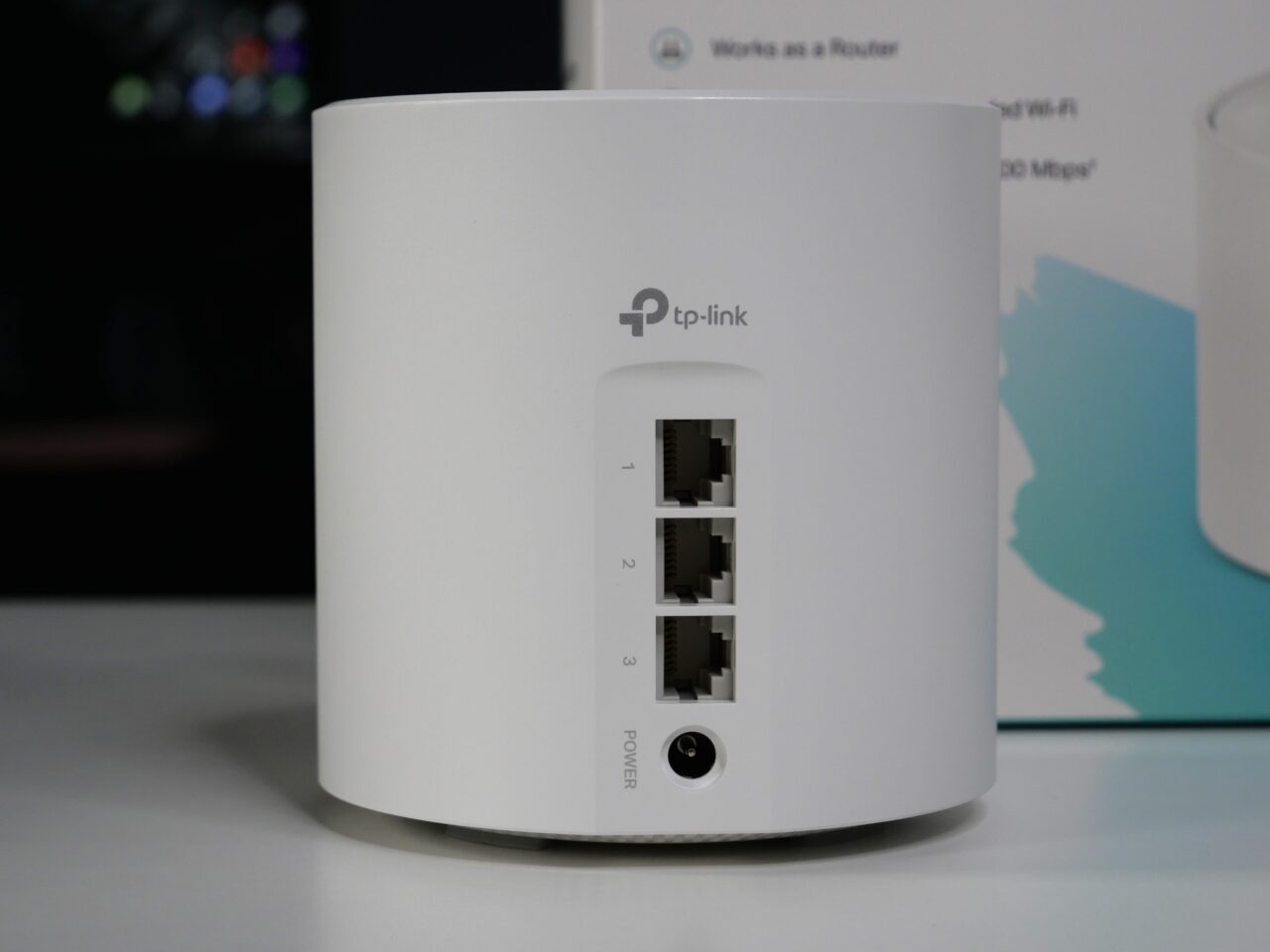 Biały router TP-Link stojący na blacie z widocznymi trzema portami Ethernet i przyciskiem zasilania.