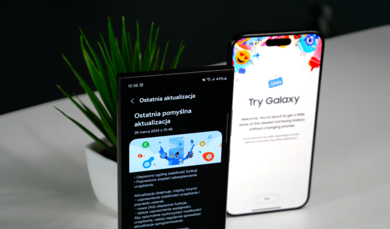 Dwa smartfony Samsung znajdujące się na biurku, jeden z ekranem wyświetlającym stronę aktualizacji systemu, drugi z promocją "Try Galaxy", w tle doniczka z zieloną rośliną.