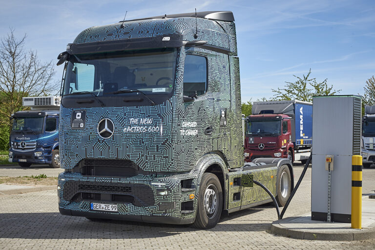 Ciężarówka Mercedes eActros 600 w maskującym oklejeniu podłączona do stacji ładowania na parkingu dla ciężarówek.