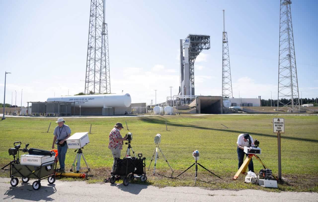Starliner - przygotowania do startu Fotografowie z agencji prasowej pracują na tle platformy startowej z wyrzutniami rakietowymi i zbiornikami ciekłego azotu na kosmodromie.