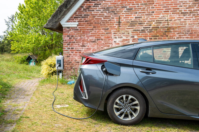 Samochód elektryczny ładuje baterię przy domowej stacji ładowania, zaparkowany obok ceglanej stodoły.
