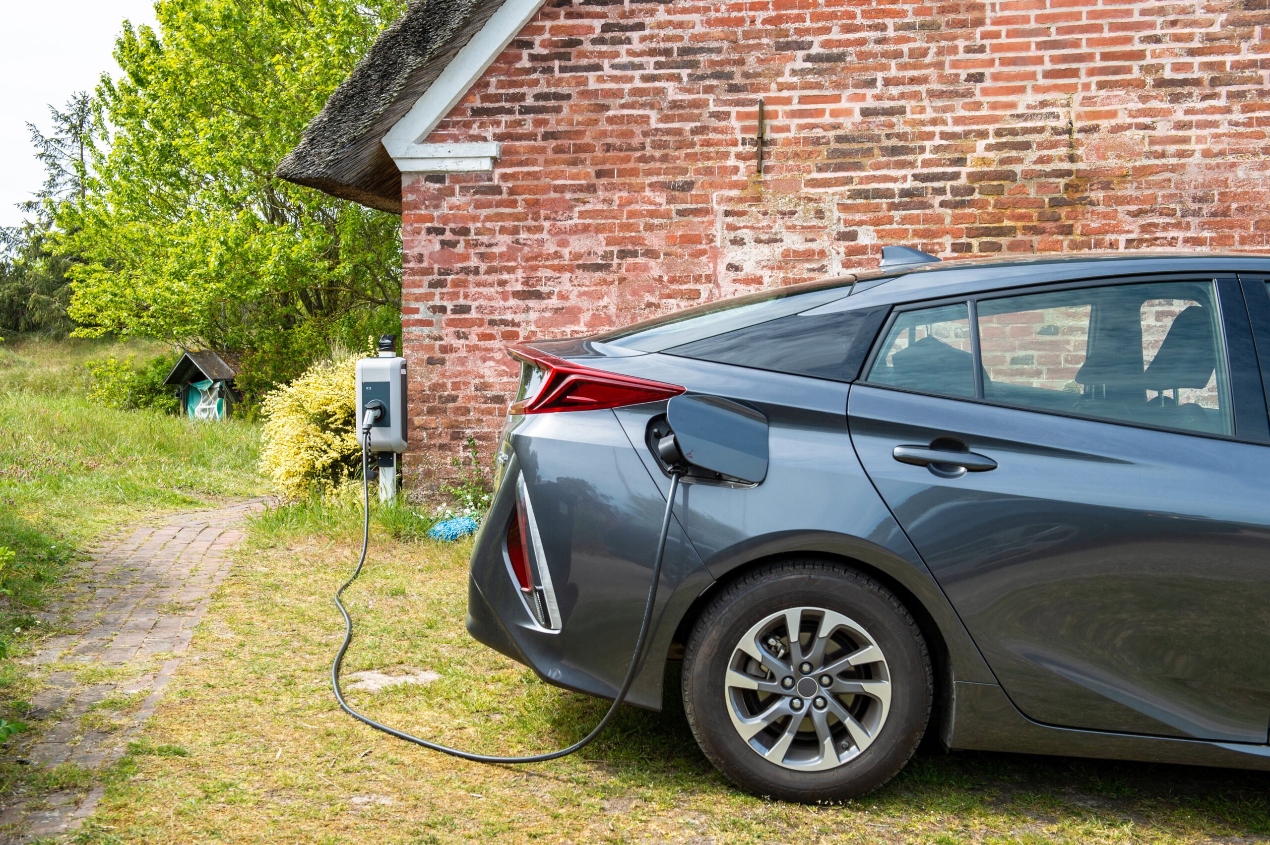 Samochód elektryczny ładuje baterię przy domowej stacji ładowania, zaparkowany obok ceglanej stodoły.
