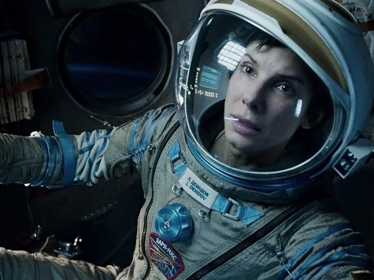 Sandra Bullock filmy. Astronautka w kombinezonie kosmicznym patrzy przed siebie, znajdując się wewnątrz statku kosmicznego.