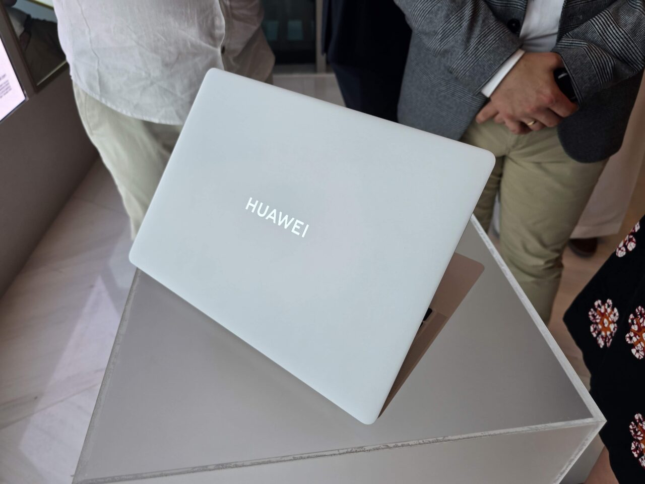 Laptop Huawei MateBook X Pro 2024 colocado sobre uma mesa cinza, duas pessoas ao fundo.