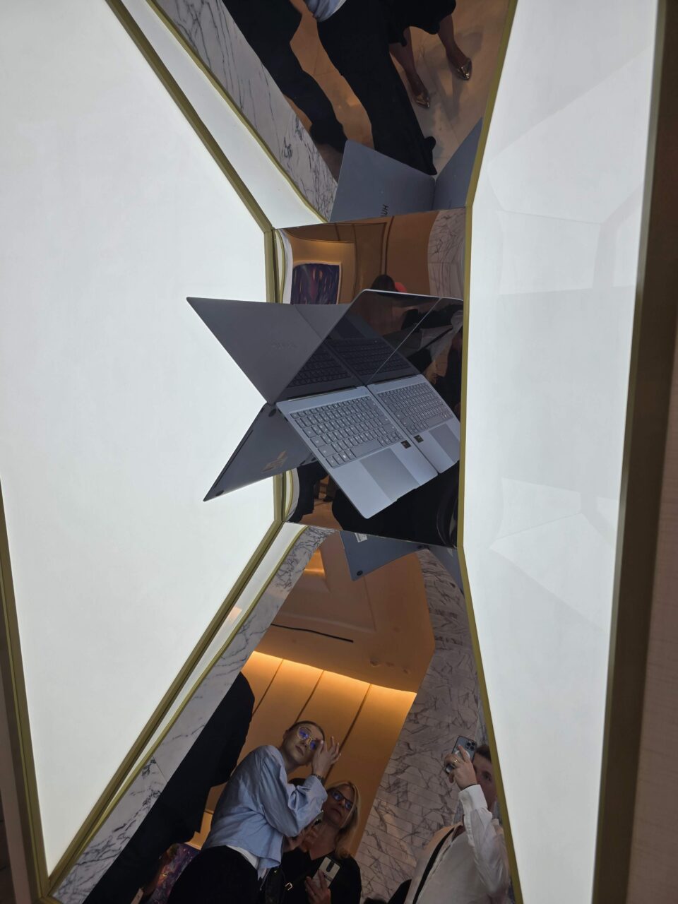 Uma foto tirada dentro de um prédio, mostrando um grupo de pessoas e laptops Huawei MateBook X Pro 2024 abertos virados de cabeça para baixo, refletidos em superfícies espelhadas, dando a impressão de estarem suspensos no ar.