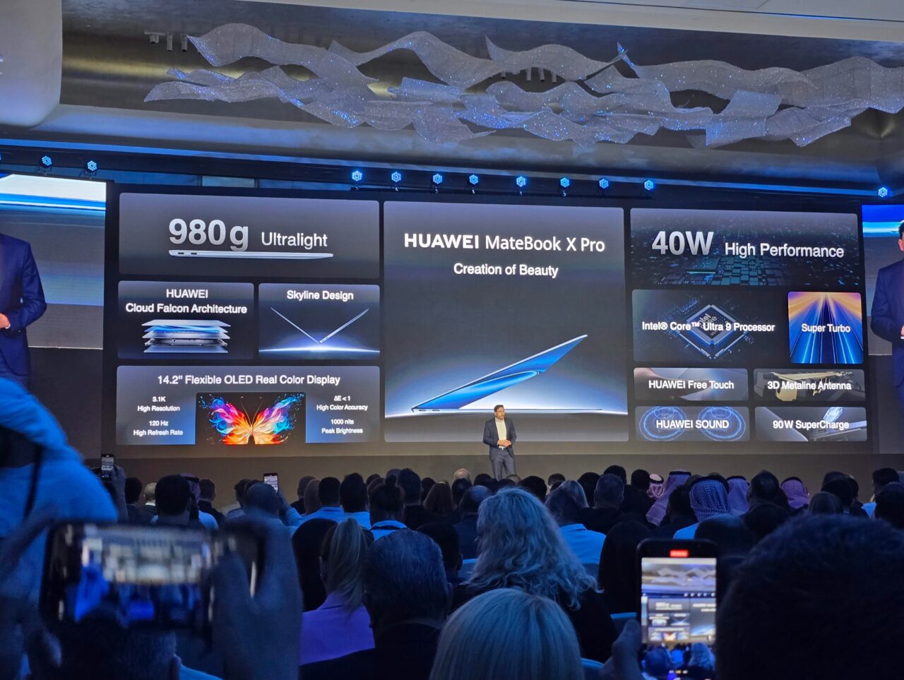 Apresentação do laptop Huawei MateBook X Pro 2024 em uma conferência, um homem no palco, uma multidão assiste à apresentação, um display com informações do produto ao fundo.