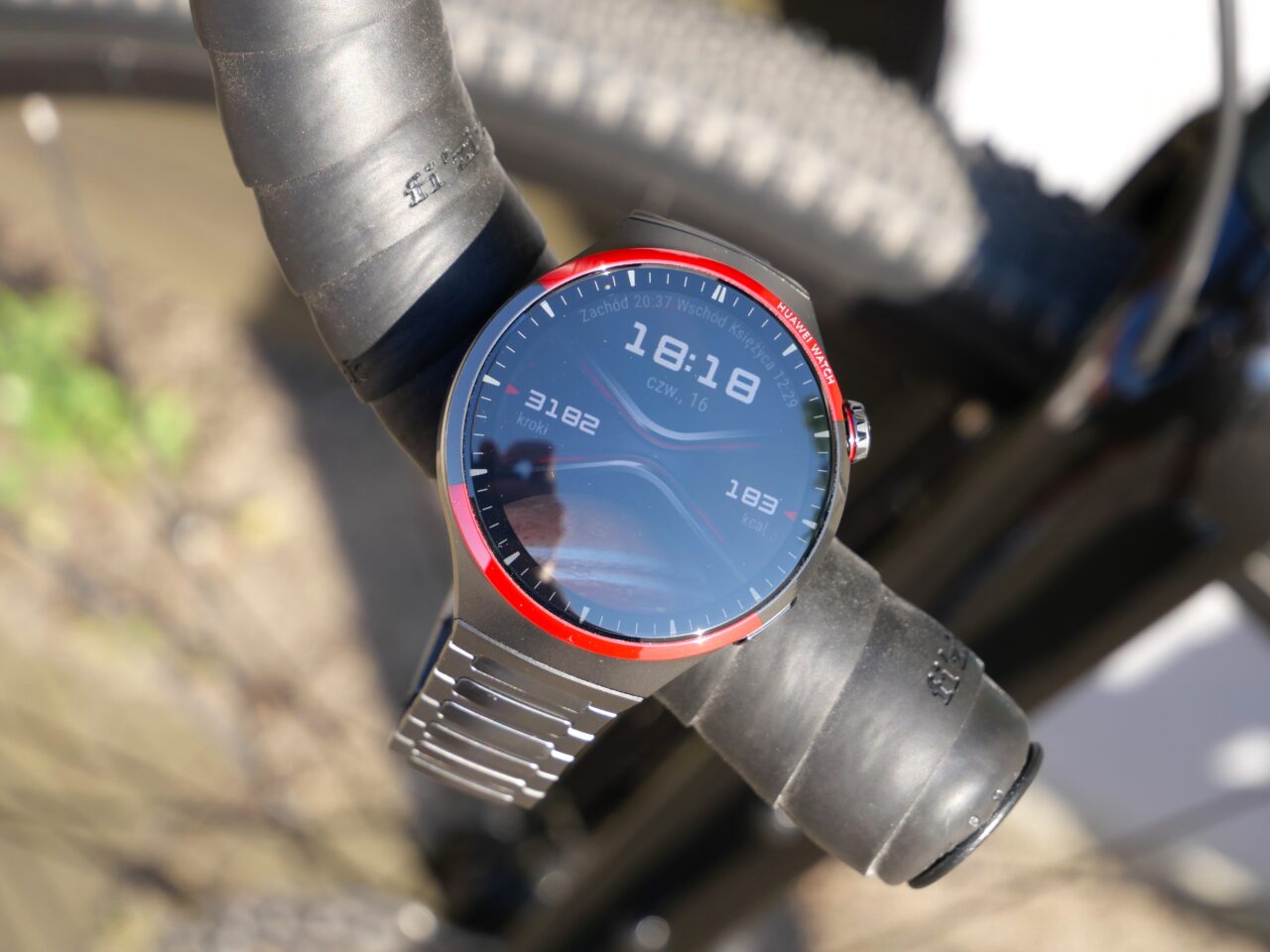 Smartwatch z metalową bransoletą, zamontowany na kierownicy roweru.