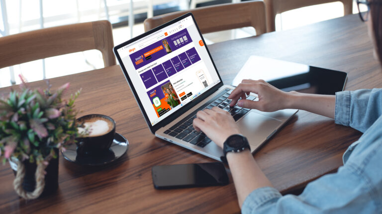 Osoba korzystająca z laptopa w kawiarni, na ekranie strona internetowa z reklamami i ofertami.