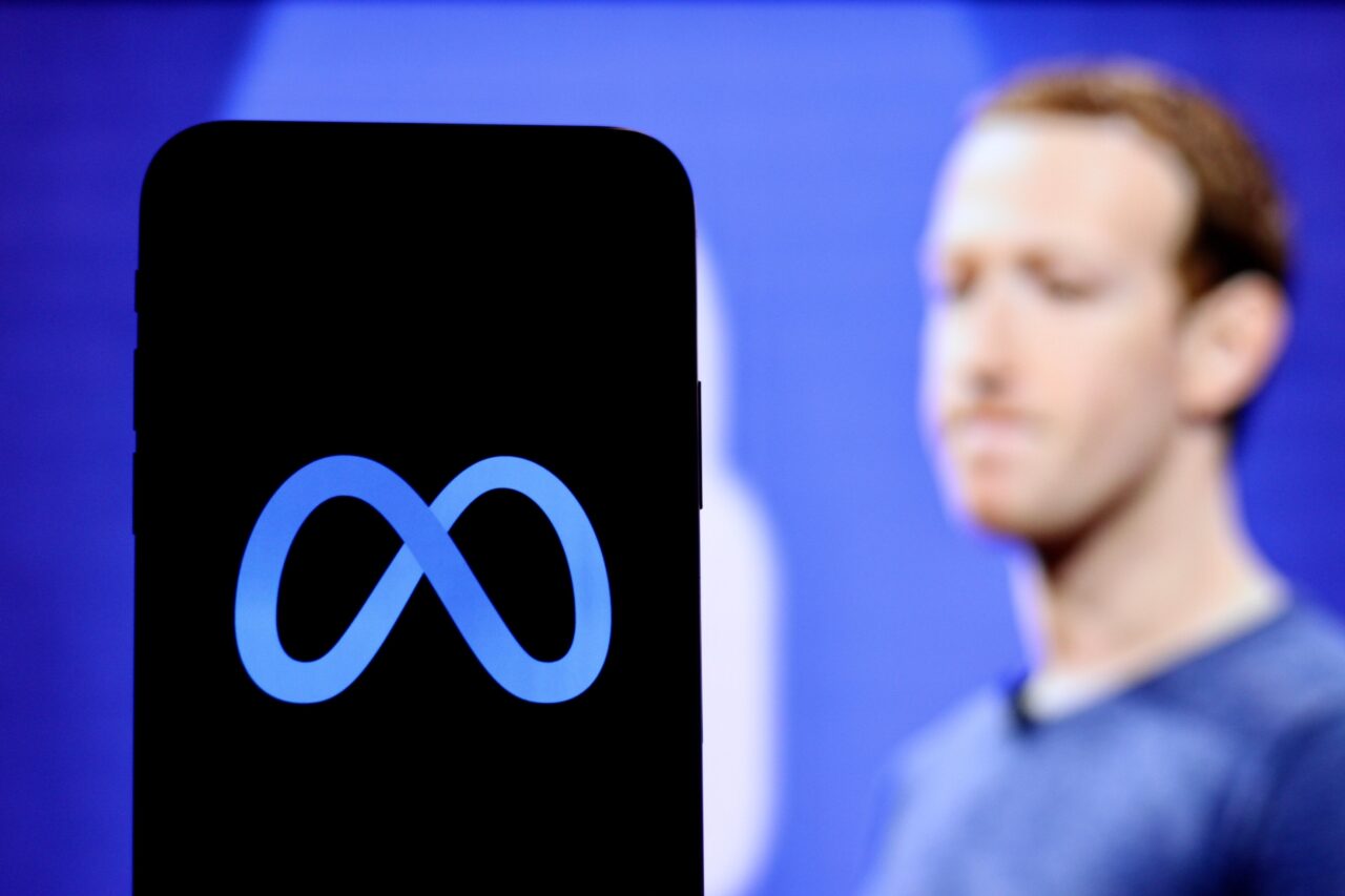 Logo Meta na ekranie smartfona, w tle rozmazana postać mężczyzny.