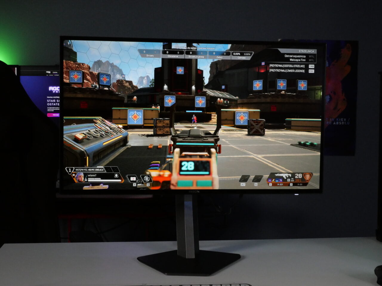 Monitor komputerowy wyświetlający grę wideo w stylu strzelanki, ustawiony w pomieszczeniu z kolorowym oświetleniem LED.