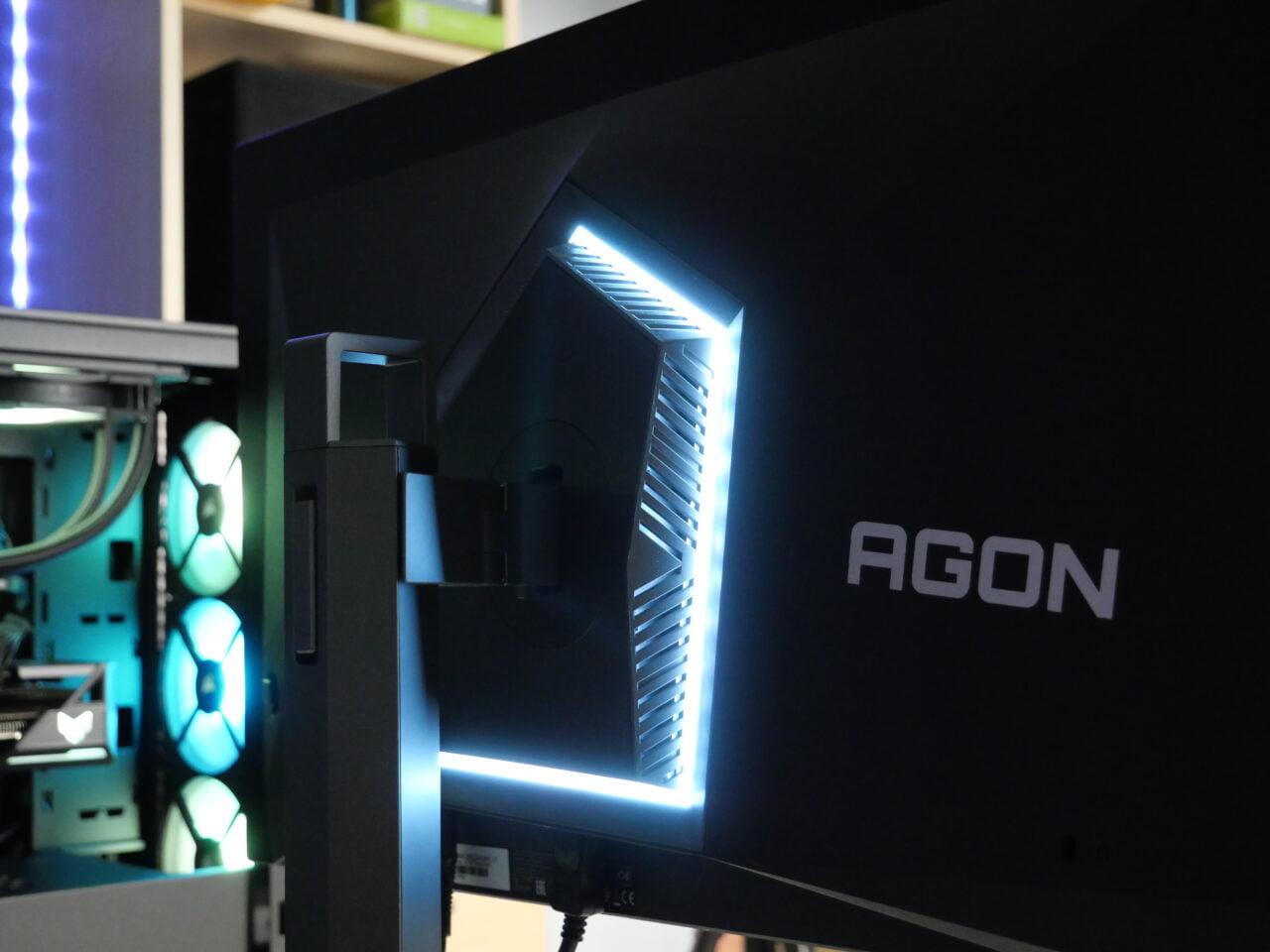 Monitor gamingowy marki Agon z podświetleniem LED, widoczny tył monitora i elementy komputera gamingowego w tle.
