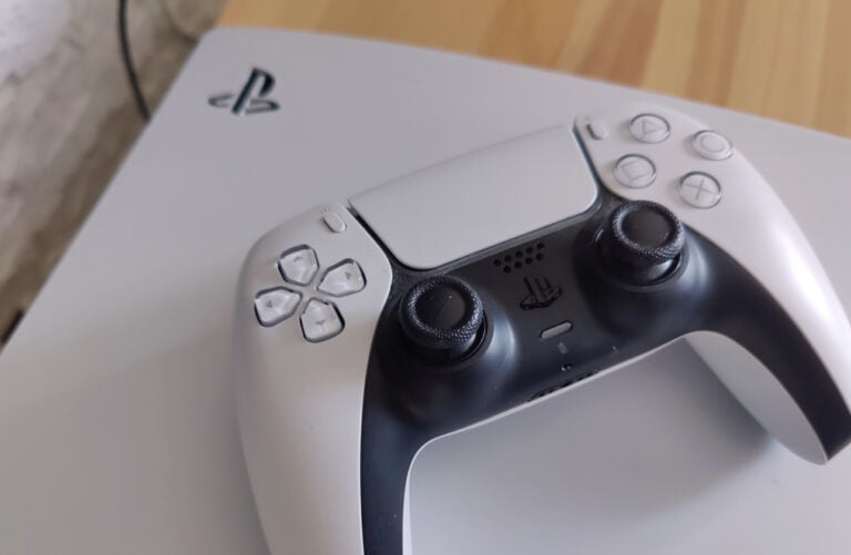 Biały kontroler do konsoli PlayStation 5, leżący na konsoli.